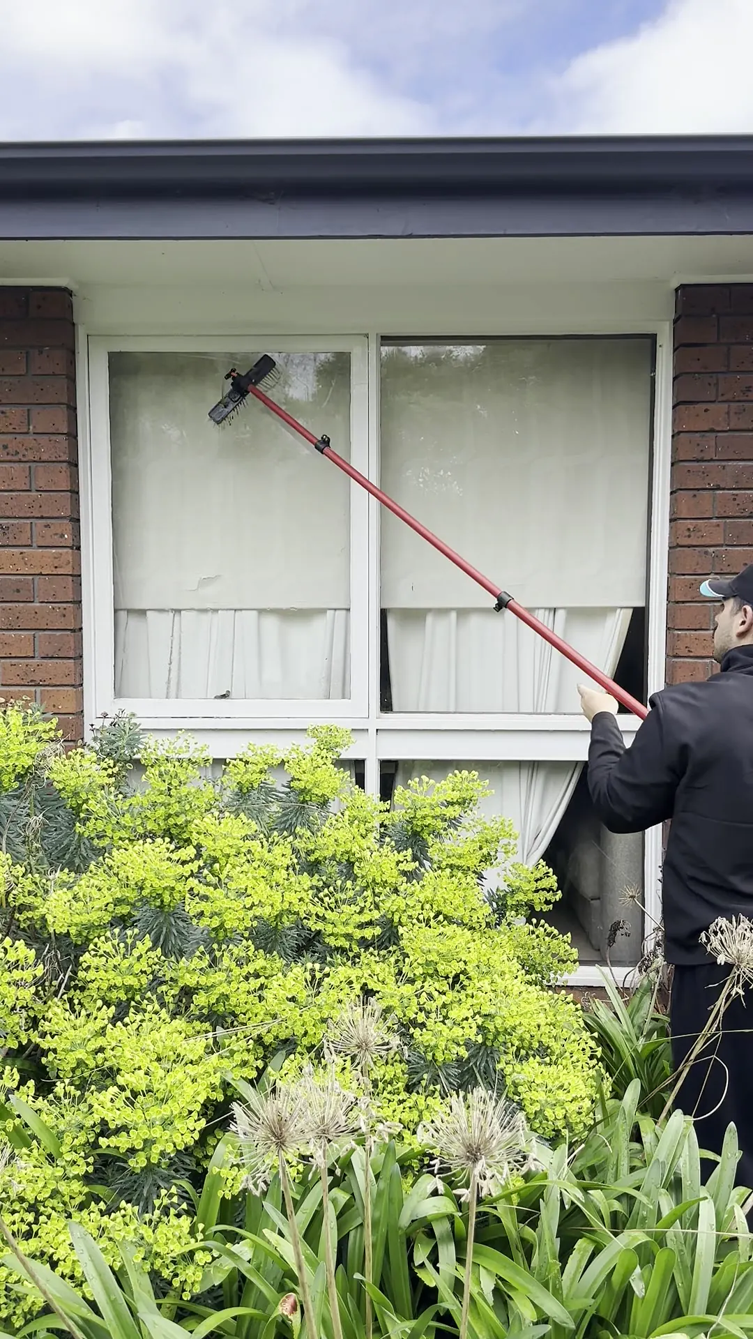 Cleaner using a water-fed pole on ribbon windows of a brick home under clear sky