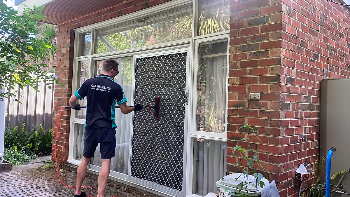 Cleaner in branded polo using a water-fed pole on the windows of a red brick home