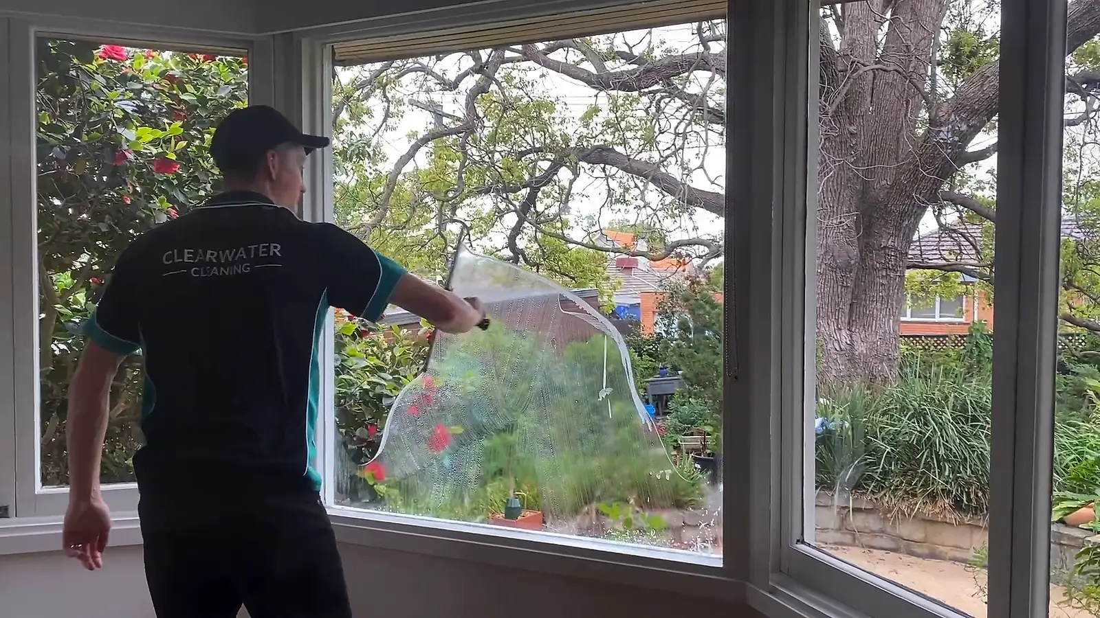 Clearwater cleaner drawing a squeegee across a bay window from inside