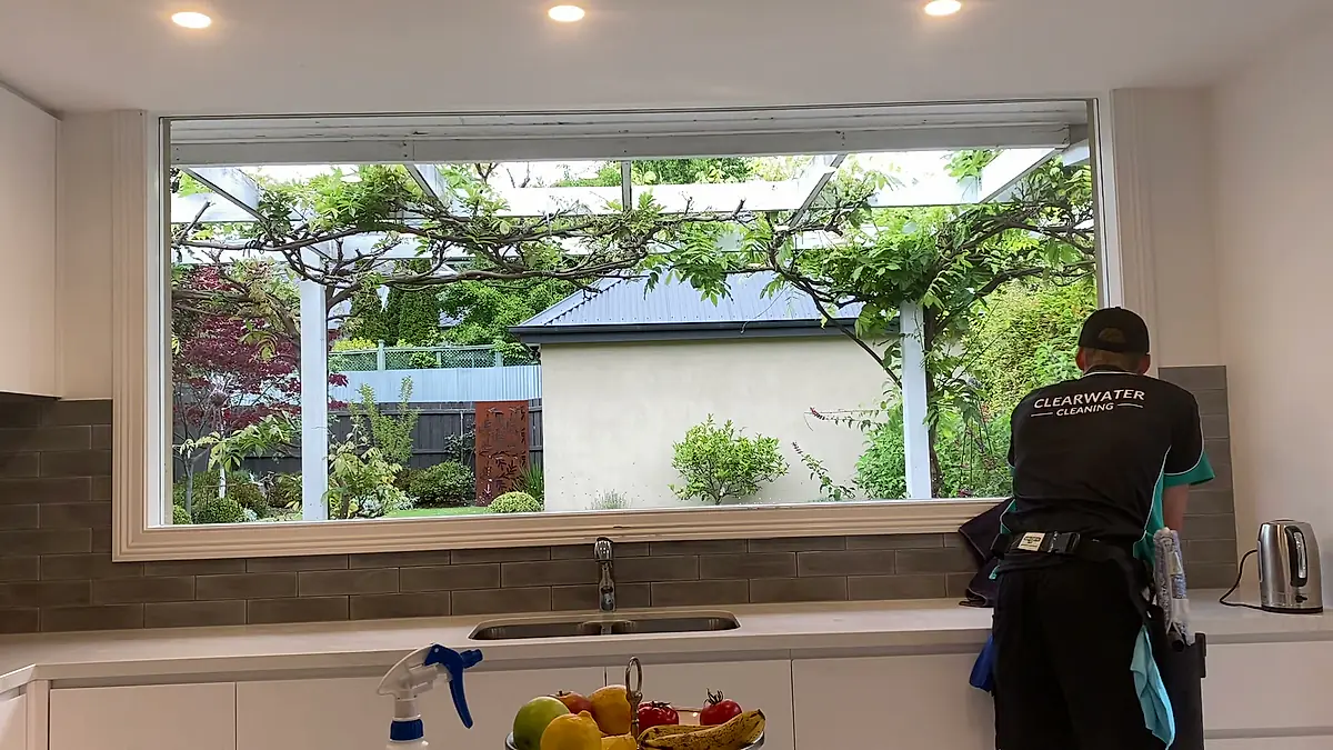 Cleaner working along a wide kitchen window during a scheduled visit