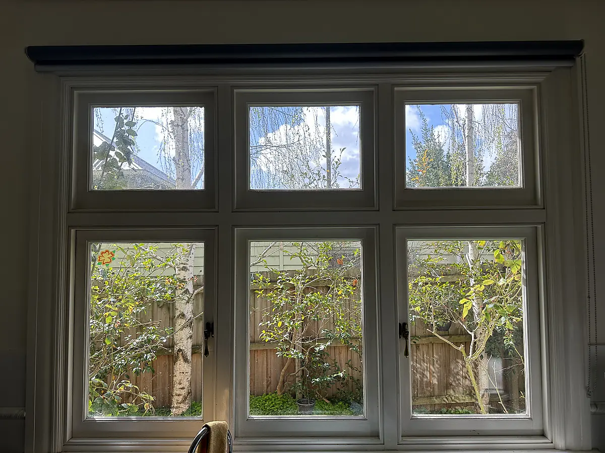 Interior of a period timber window before cleaning, the glass spotted and hazy against the garden outside