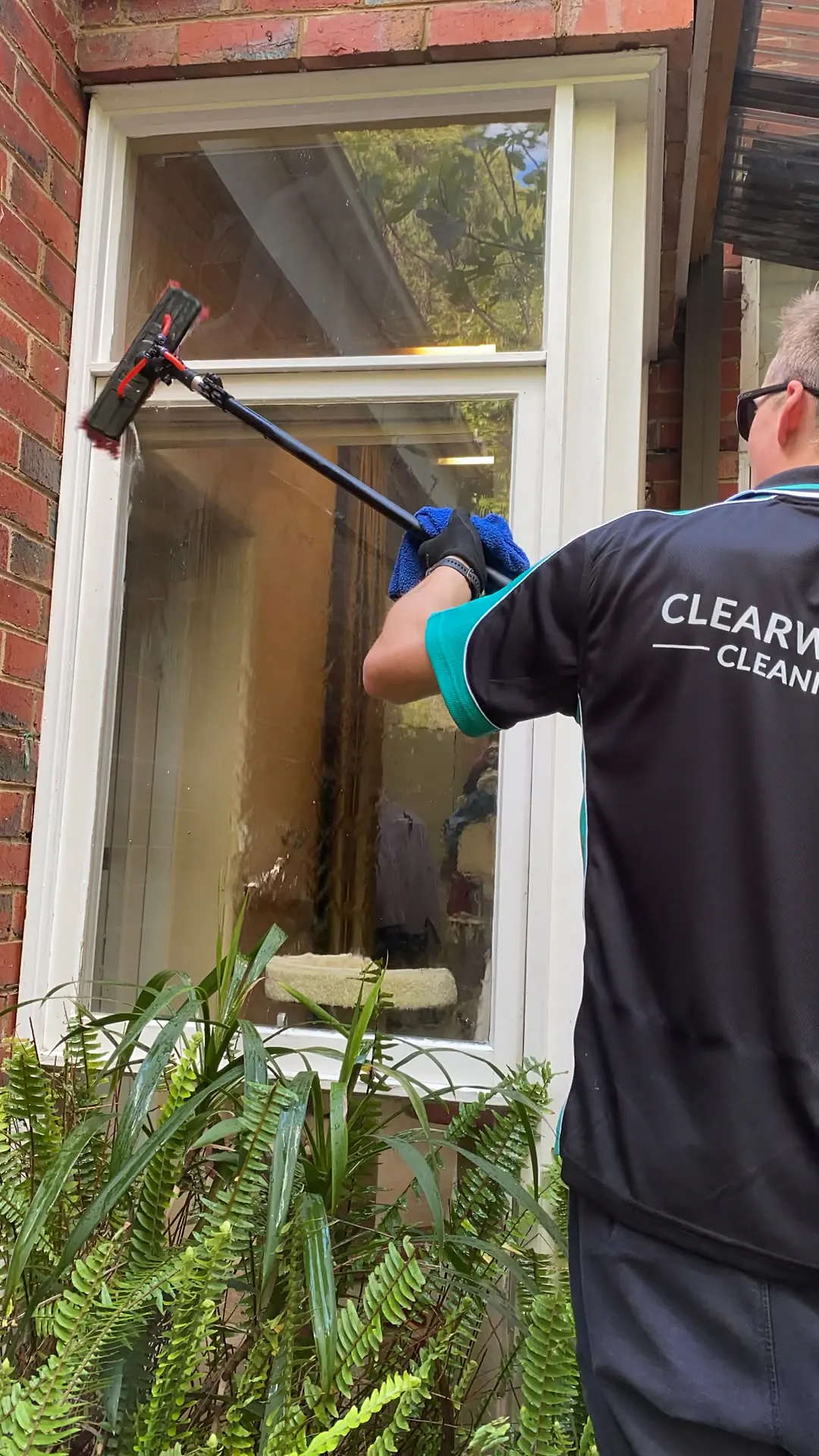 Cleaner working a pole across a timber sash window on a period red brick home
