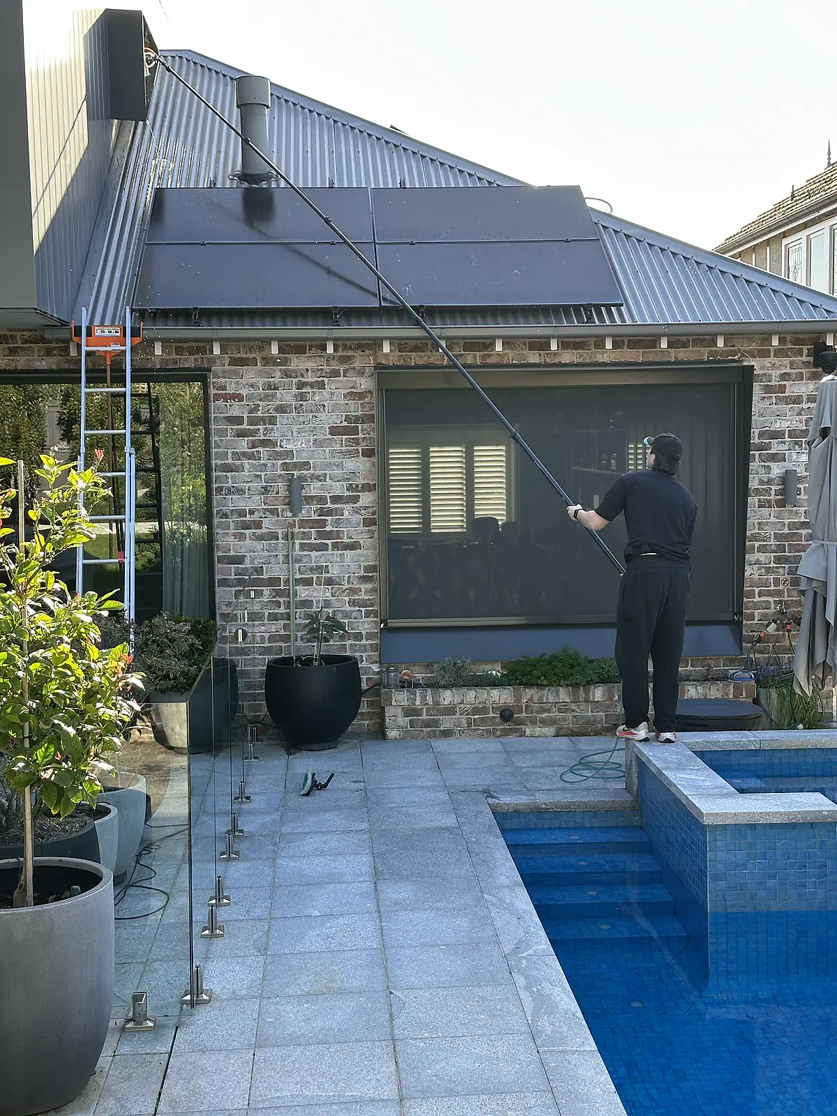 Frameless glass pool fence in the foreground, clear enough to see the pool tiles through it, with a Clearwater cleaner working beyond it