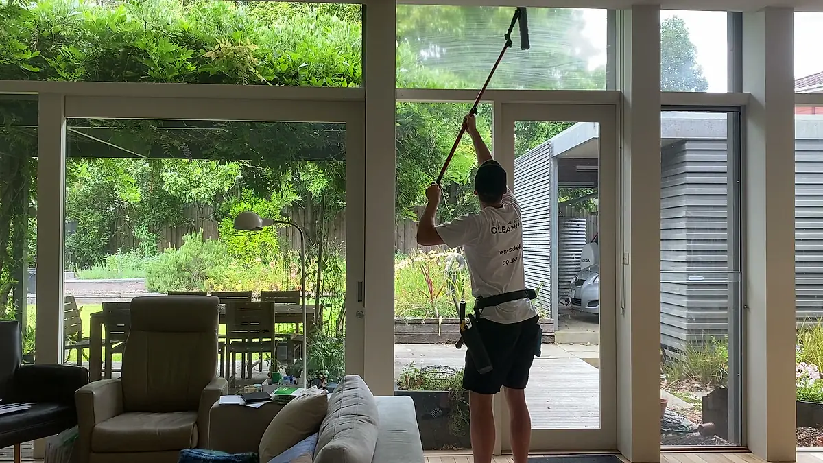 Cleaner using a pole on a full-height interior glass wall
