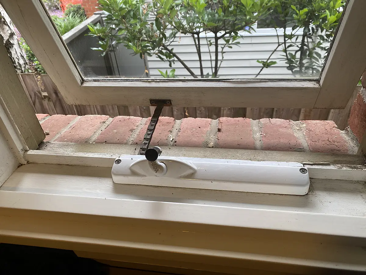 Grit and debris built up in a window track and along the sill, with paint flaking from the timber frame